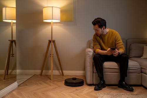 robotdammsugare som städar medan en man i gul tröja sitter i soffan och tittar på den